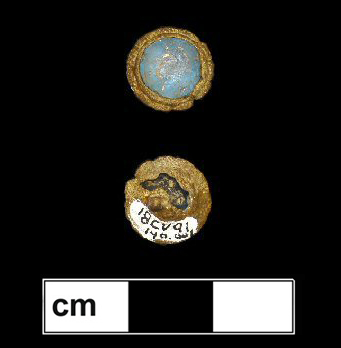 Blue faceted glass jewel in a copper alloy setting with a decorative crimped rim. 